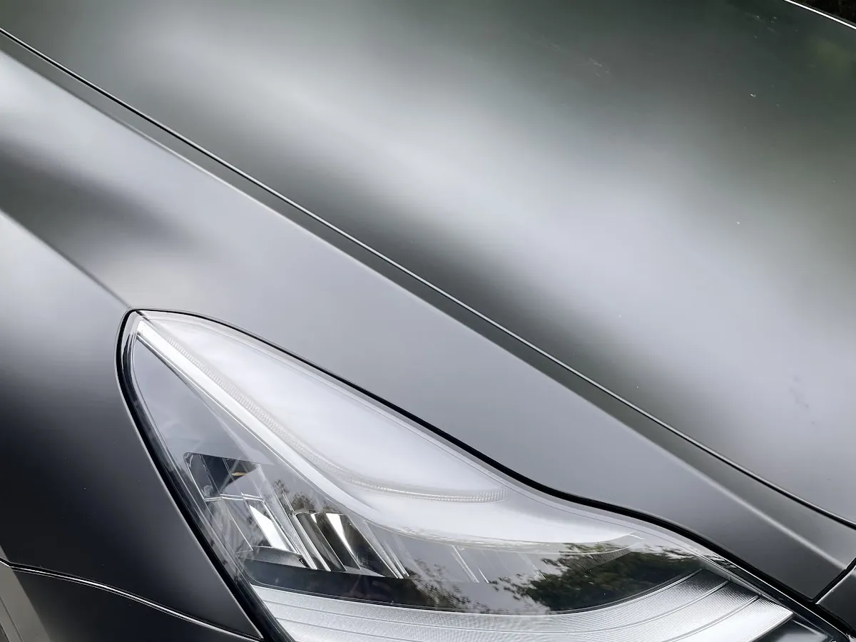 Satin black vinyl wrap on a Tesla headlight and fender